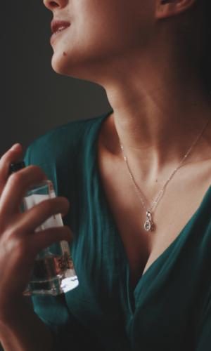 A vertical shot of a female wearing a necklace with a diamond pendant spraying perfume on her